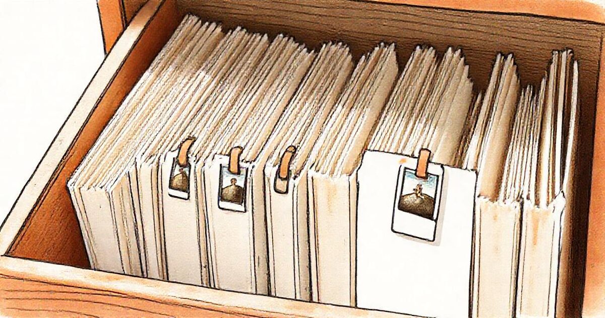 A wooden file drawer of paper folders, each with a small photo clipped to the front