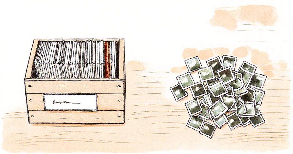 Tidy labelled folders in a wooden crate beside a loose scattered pile of small photo prints